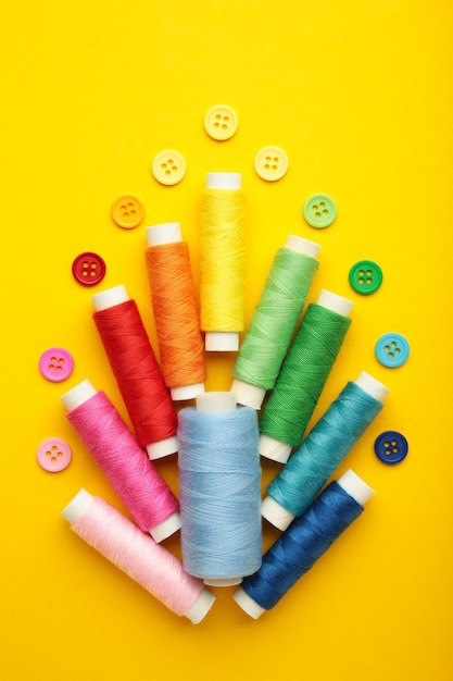 Colorful buttons with colorful thread on yellow background Vertical photo