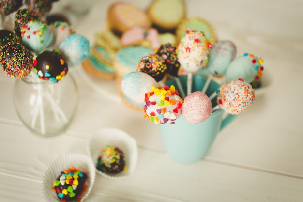 Colorful cake pops in cups on white wooden desk