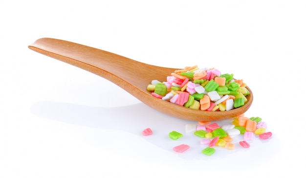 Colorful candy in wood spoon on white wall