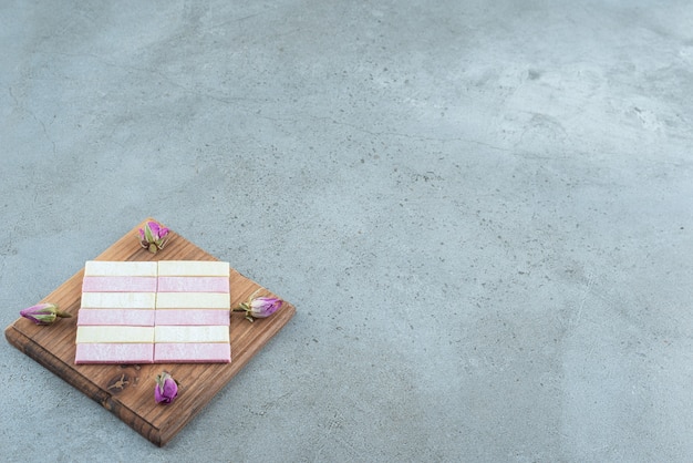 Colorful chewing gums with dried roses on wooden board.