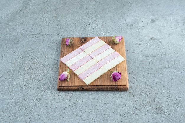 Colorful chewing gums with dried roses on wooden board.