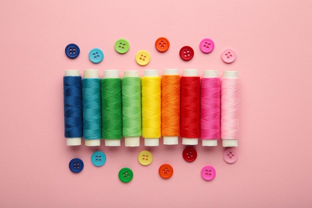 Colorful cotton yarns on rolls for sewing on pink background