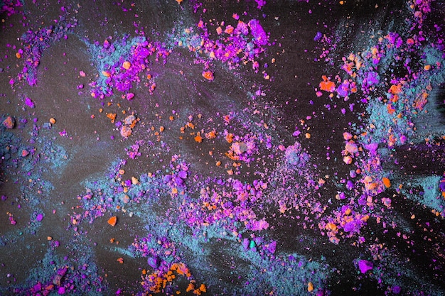 Colorful crumbled holi powder colors on black background Flat lay