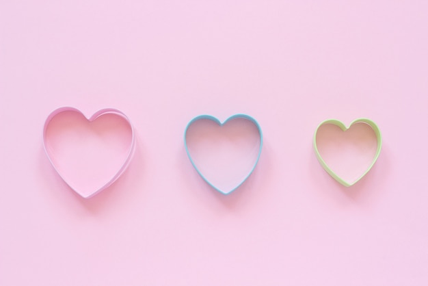 Colorful cutters cookies in heart shape on pastel pink background. Concept Valentine's card.