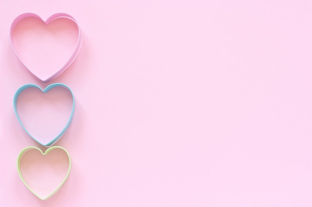 Colorful cutters cookies in heart shape on pastel pink background