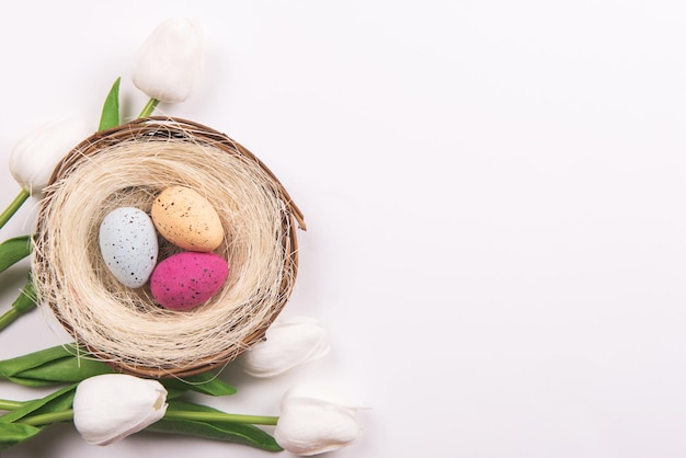 Colorful decorations with Easter egg nest and tulip flowers on white background. copy space, top view