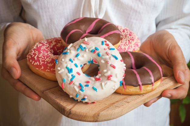 Colorful donuts on a plate are served in your hands.