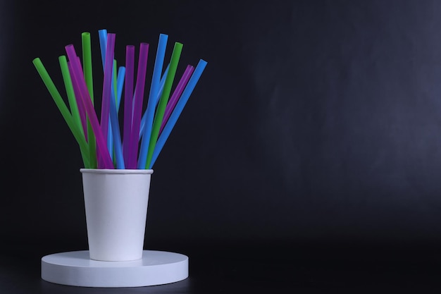 Colorful drinking plastic straws with disposable paper cup on dark background. Copy space