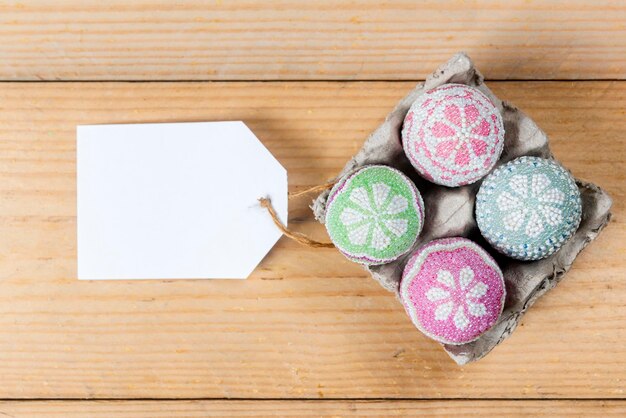 Colorful easter egg on egg tray with an empty tag on a wooden table Happy Easter