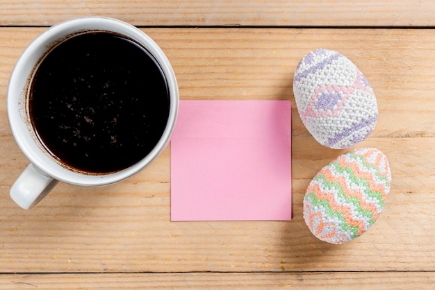 Colorful easter egg with empty notepaper and cup of coffee on a wooden table Happy Easter