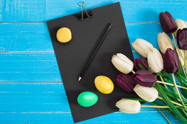 Colorful easter eggs and bouquet of tulips on wooden background with space for a text