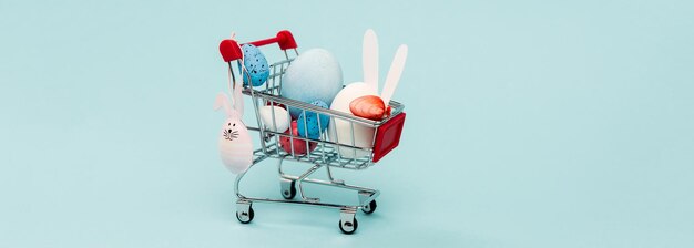 Colorful easter eggs and decorative rabbits in cart on blue panoramic shot