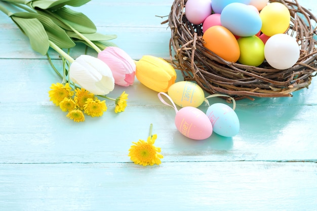 Colorful Easter eggs in nest with flowers on blue wooden background.