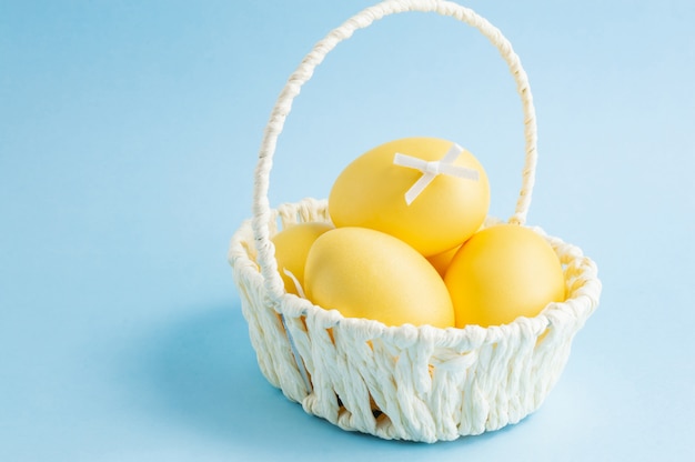 Colorful Easter eggs in a white basket on blue background.