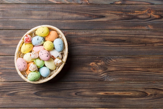 Colorful Easter eggs in wicker basket against colored background closeup top view with copy space