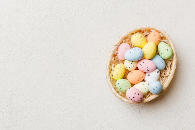 Colorful Easter eggs in wicker basket against colored background closeup top view with copy space