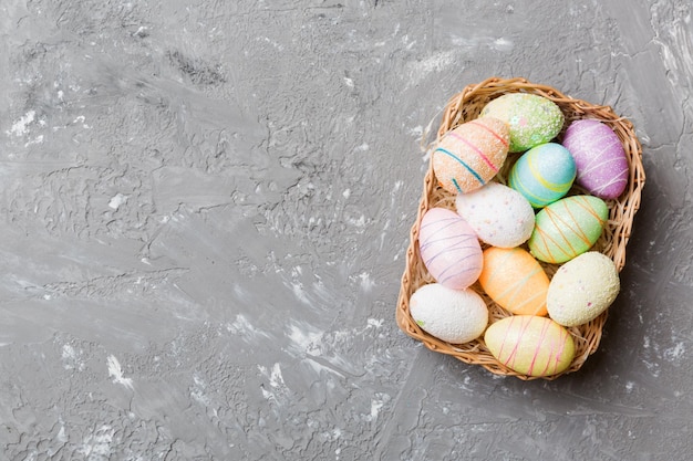 Colorful Easter eggs in wicker basket against colored background closeup top view with copy space