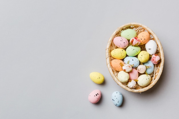 Colorful Easter eggs in wicker basket against colored background closeup top view with copy space