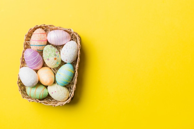 Colorful Easter eggs in wicker basket against colored background closeup top view with copy space