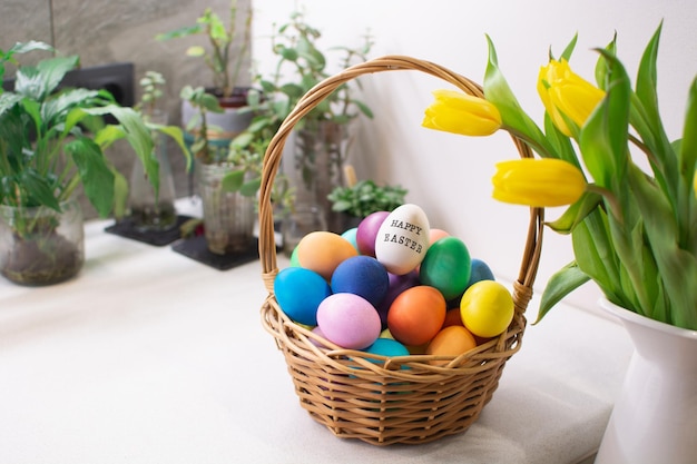 Colorful easter eggs in wicker basket on table in kitchen interior with tulips