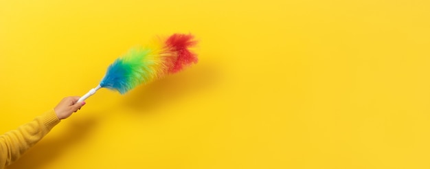 Colorful feather duster in hand on yellow