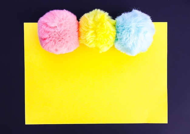 Photo colorful fluffy pompons on bright yellow background. fashion decoration festive template. design element for poster, banner, web, greeting card.