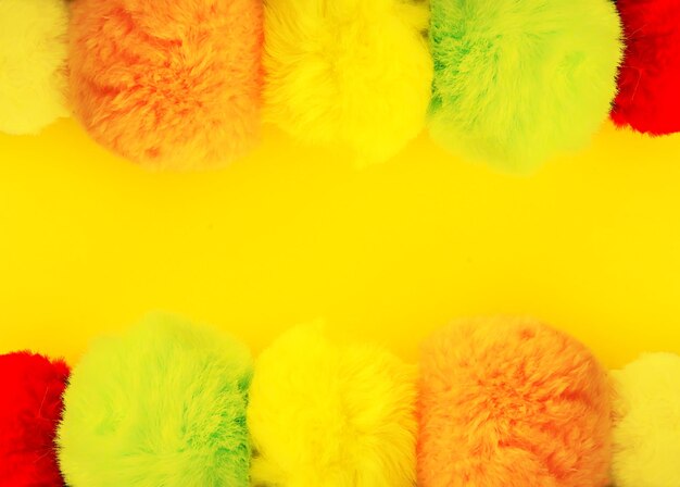 Photo colorful fluffy pompons on bright yellow background. fashion decoration festive template. design element for poster, banner, web, greeting card.