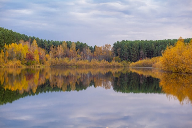 Colorful foliage tree reflections in calm pond water on a beautiful autumn day. A quiet and beautiful place to relax.