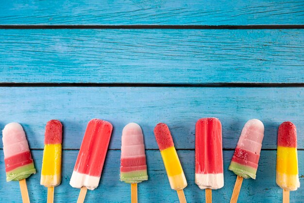 Photo colorful fruit ice cream stick look fresh to eat placed on a blue vintage wooden