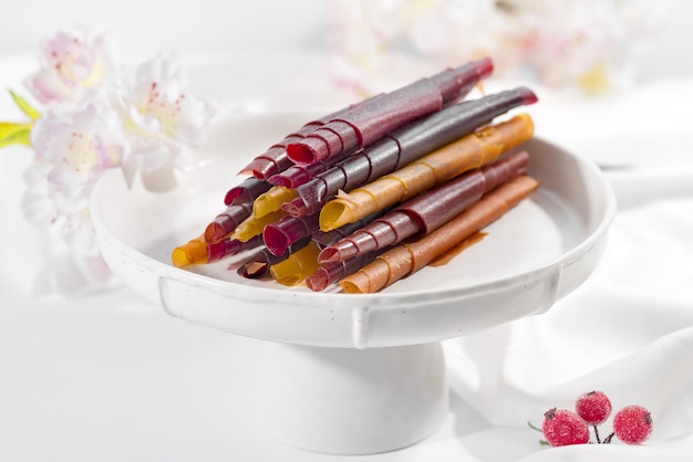 Colorful fruit leather rolls on a plate on light background