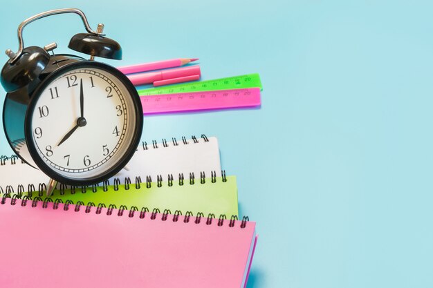 Colorful girlish school supplies, book and alarm clock on punchy blue. Close up. Back to school.