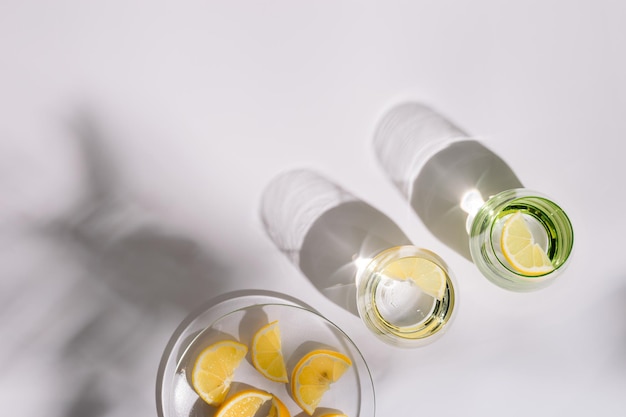 Colorful glass cups with fresh water and plate with slices of lemon on white background Creative