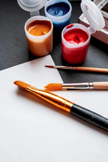 Colorful gouache paints in open plastic cans and paint brushes ready to drawing