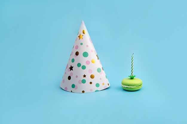 Colorful Hat for Party and green Macaroon with a candle on a blue