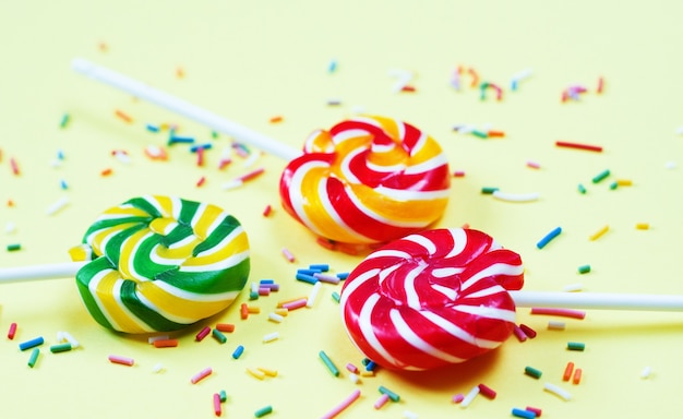 Colorful lollipops and confetti on yellow background. Sweets for party. Sugar