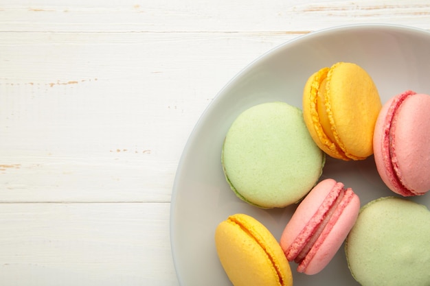 Colorful macarons cakes on grey plate on white wooden background. Small French cakes on plate.