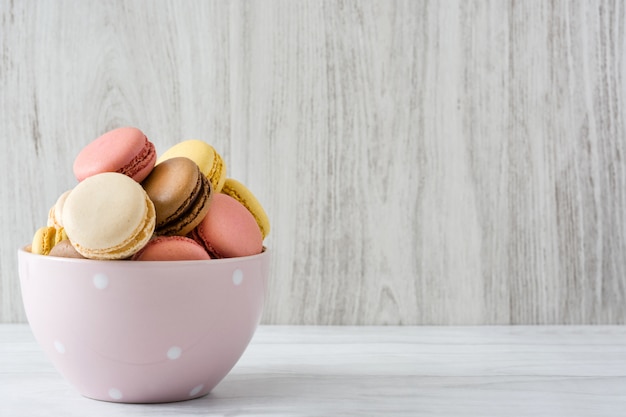 Colorful macarons in a vintage bowl on white wooden table