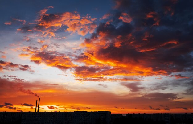 Colorful Magic Sunset. Roofs of city houses during sunrise. Birds flying in the sky. Dark smoke coming from the thermal power plant pipe.