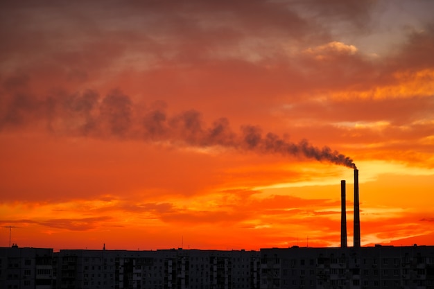 Colorful Magic Sunset. Roofs of city houses during sunrise. Dark smoke coming from the thermal power plant pipe.