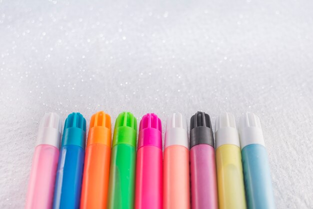 Colorful markers on white background with glitter.