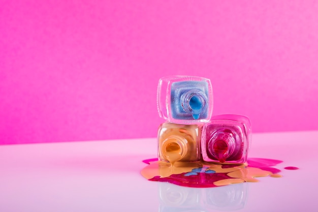 Colorful nail polish spilled on pink backdrop