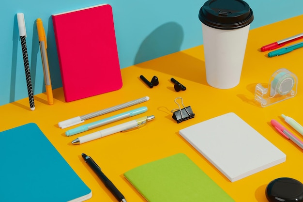 Colorful notepads pens and paper cup on orange table