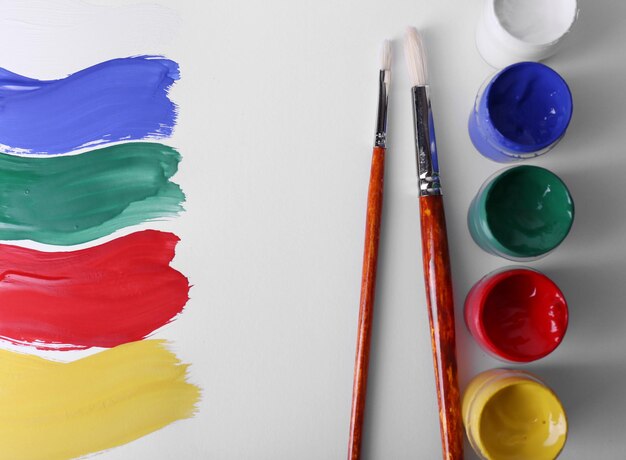 Colorful paint strokes with brush and paint cans on white sheet of paper background