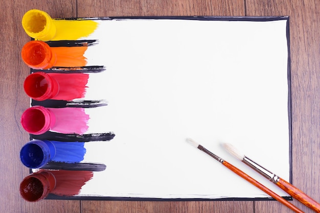 Colorful paint strokes with brush and paint cans on white sheet of paper on wooden table background