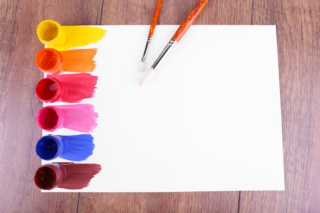 Colorful paint strokes with brush and paint cans on white sheet of paper on wooden table background