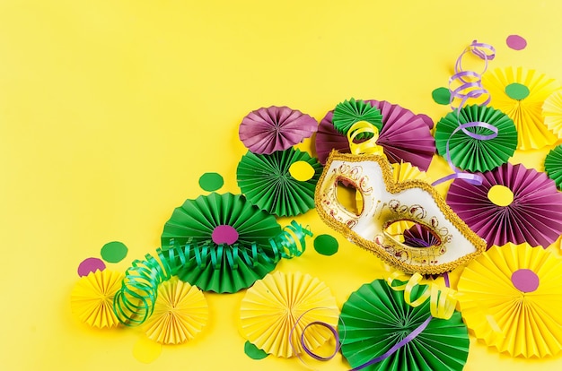 Colorful paper confetti, carnivale mask and colored serpentine on a yellow background