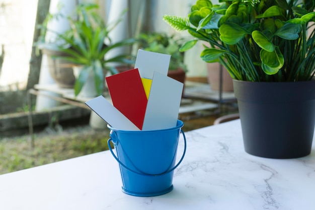 Colorful paper inside of a blue bucket on a white table with garden background