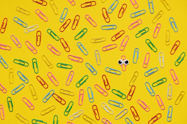 Colorful paperclips on yellow background and only one under magnifying glass