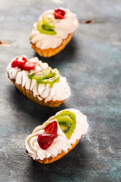 Colorful pastry cakes with chantilly cream, fruits and berries on grunge blue wooden background