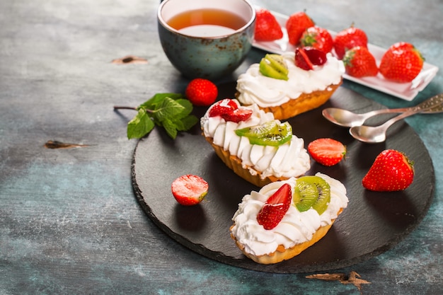 Colorful pastry cakes with chantilly cream, fruits and berries on grunge blue wooden background